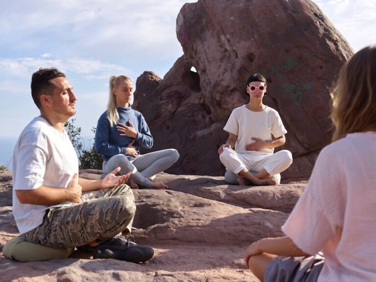 Four people meditate on rocky terrain under a clear sky, promoting serenity and mindfulness.