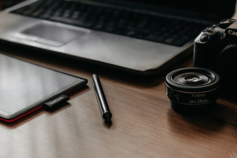 A workspace featuring a laptop, tablet, camera, and lens, ideal for creative work and photography.